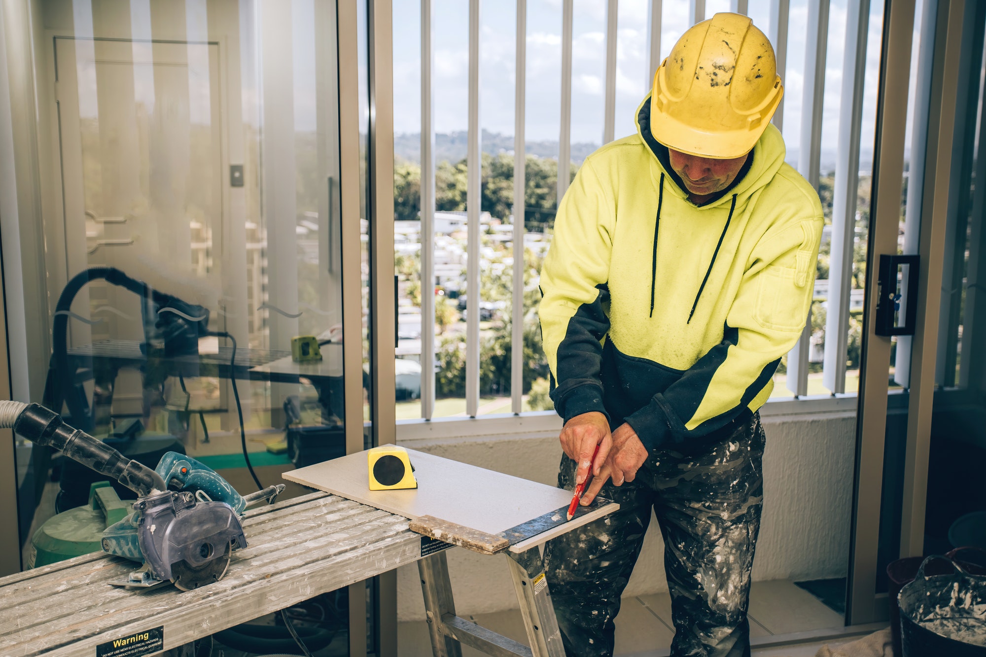 Man marking marks with pencil on a tile to be cut. Laying ceramic floor tiles, home renovation